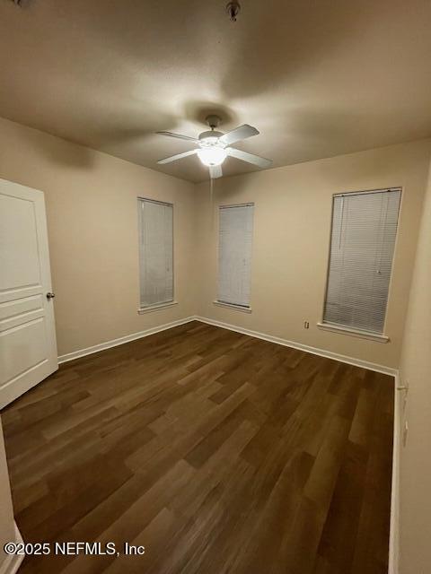 unfurnished room featuring ceiling fan, dark wood finished floors, and baseboards