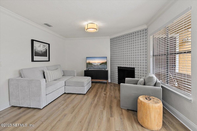 living area featuring baseboards, light wood-style flooring, visible vents, and crown molding