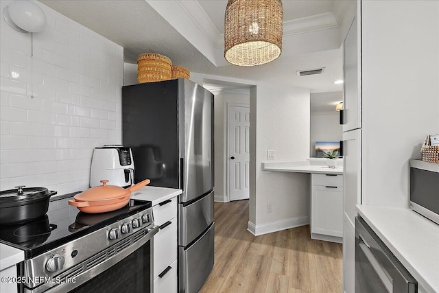 kitchen featuring light wood-type flooring, stainless steel appliances, crown molding, and light countertops