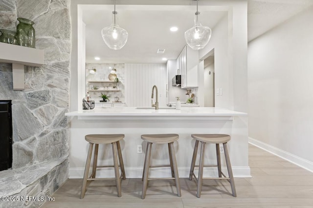 kitchen featuring stainless steel microwave, a kitchen breakfast bar, a peninsula, white cabinetry, and a sink