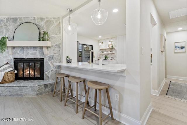 kitchen featuring wood finished floors, a fireplace, a sink, and baseboards