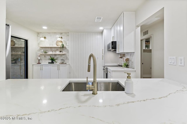 kitchen featuring stainless steel appliances, white cabinetry, a sink, and light stone counters