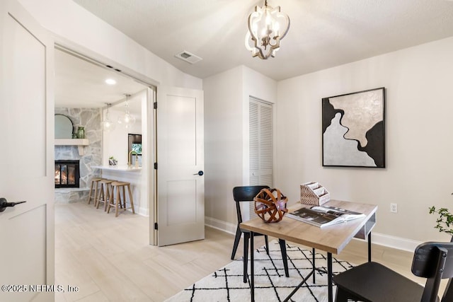 home office with baseboards, visible vents, light wood-style flooring, an inviting chandelier, and a fireplace