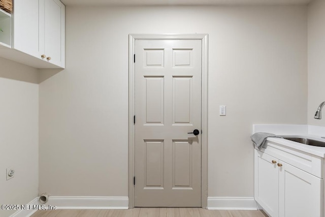 clothes washing area with cabinet space, hookup for an electric dryer, a sink, light wood-type flooring, and baseboards