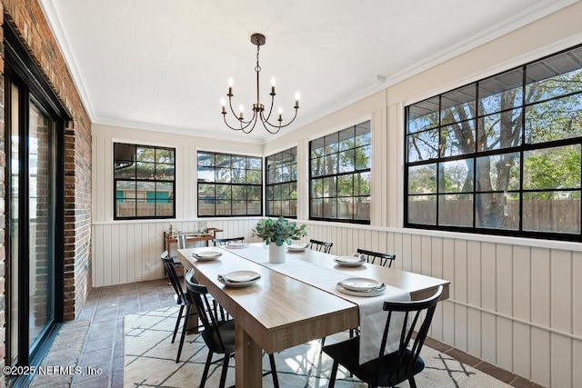 dining room with a notable chandelier, crown molding, and brick wall