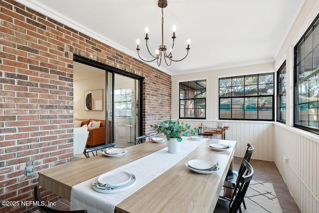 dining area featuring tile patterned flooring, brick wall, ornamental molding, wainscoting, and an inviting chandelier