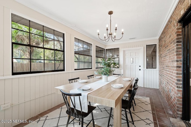 dining space with a wealth of natural light, brick wall, a chandelier, and crown molding