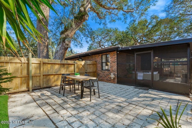 view of patio with outdoor dining space, fence, and a sunroom