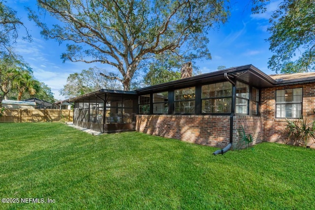 view of side of home with brick siding, a yard, a chimney, a sunroom, and fence