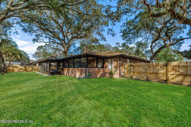 rear view of property featuring a yard, a fenced backyard, a sunroom, and brick siding