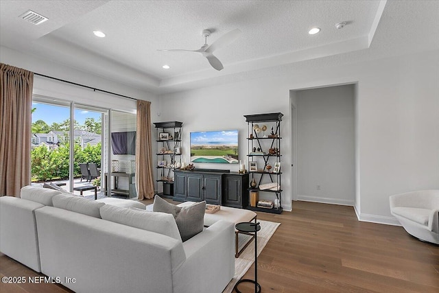 living area featuring a tray ceiling, wood finished floors, visible vents, and baseboards