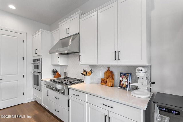 kitchen with under cabinet range hood, white cabinetry, appliances with stainless steel finishes, and backsplash