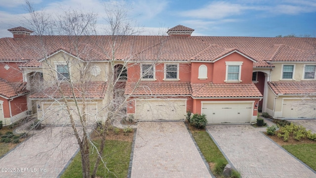 view of front facade featuring a garage, stucco siding, decorative driveway, and a tiled roof