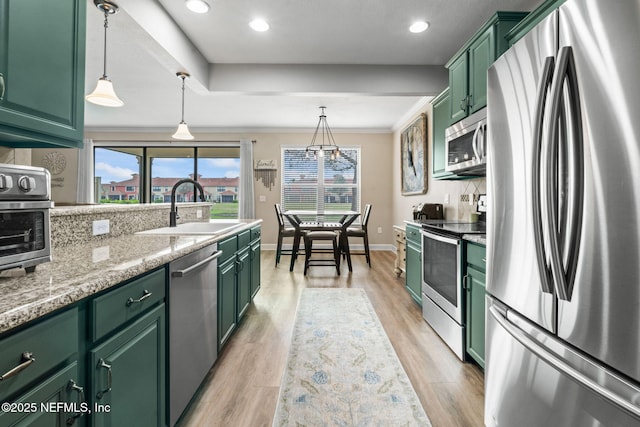 kitchen with stainless steel appliances, a sink, light wood-style flooring, and green cabinets