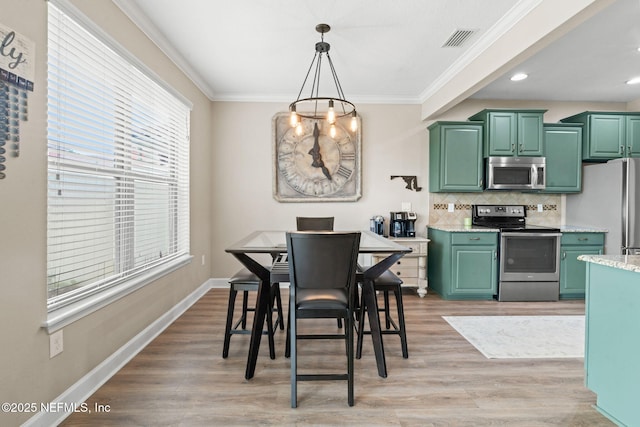 dining space with baseboards, visible vents, light wood-style flooring, crown molding, and a chandelier