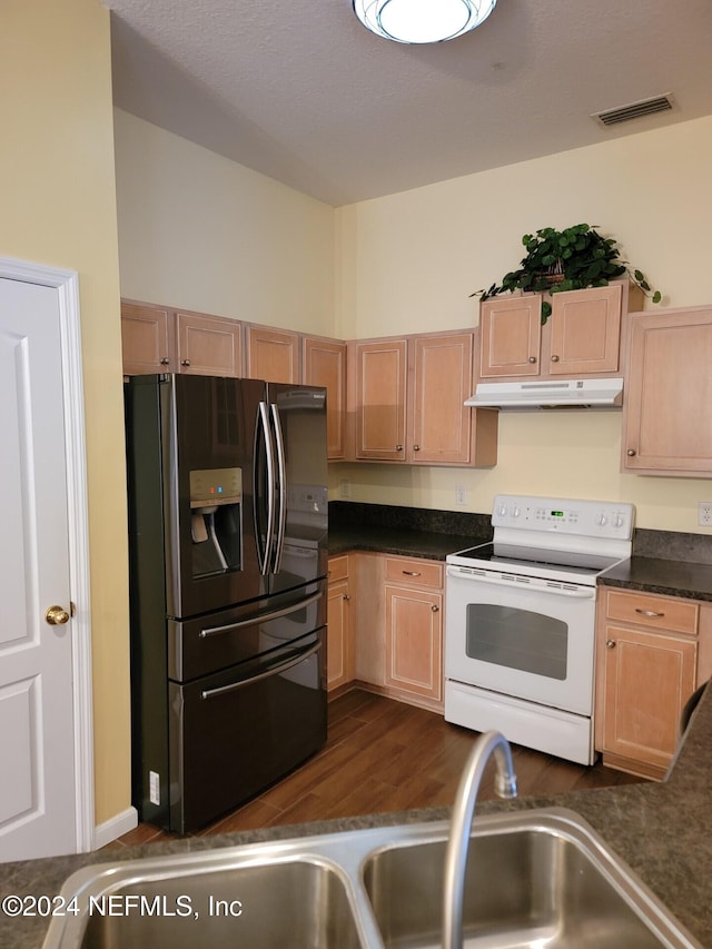 kitchen with white electric stove, visible vents, dark countertops, under cabinet range hood, and refrigerator with ice dispenser