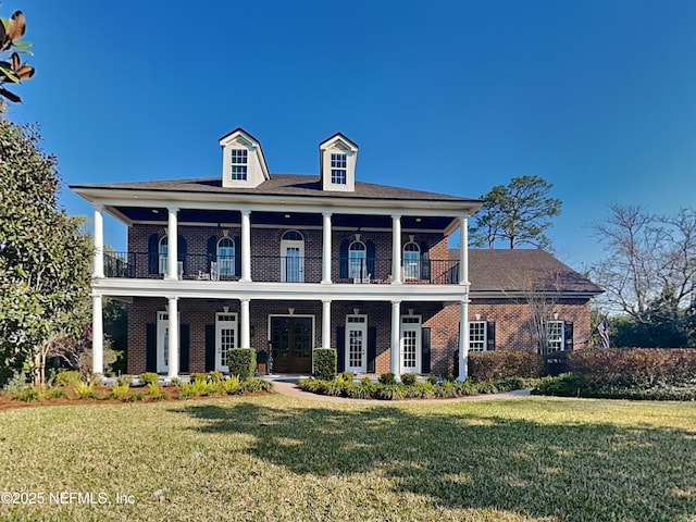 neoclassical home featuring a balcony, brick siding, a front lawn, and french doors