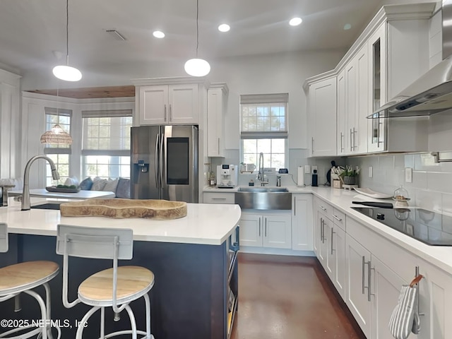 kitchen featuring stainless steel fridge with ice dispenser, light countertops, a sink, wall chimney exhaust hood, and black electric cooktop