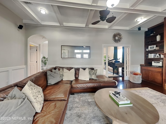 living area featuring arched walkways, ceiling fan, wainscoting, dark wood-style floors, and beamed ceiling