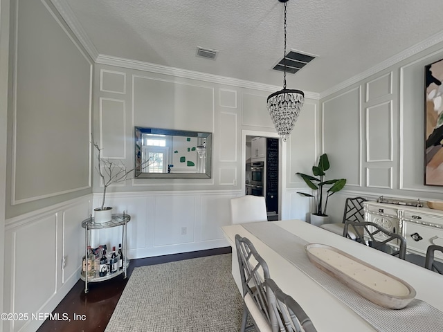 dining area featuring visible vents, dark wood finished floors, a textured ceiling, a decorative wall, and a notable chandelier