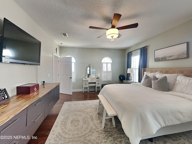 bedroom featuring baseboards, visible vents, ceiling fan, dark wood-style flooring, and a textured ceiling