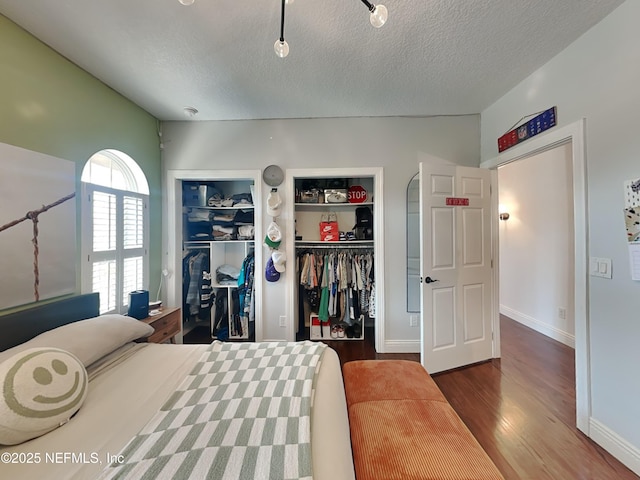 bedroom with multiple closets, a textured ceiling, baseboards, and wood finished floors