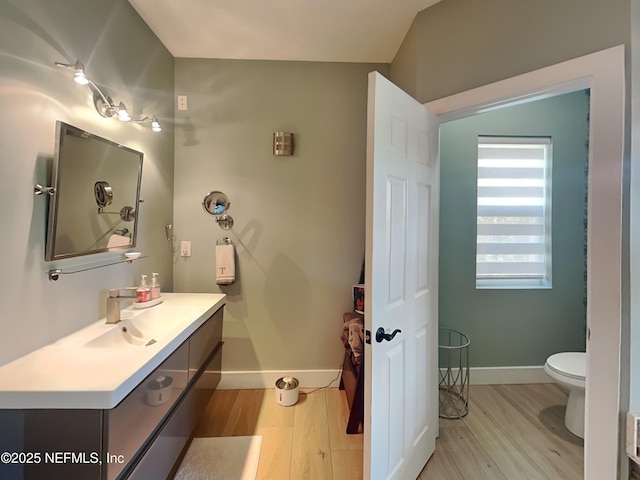 half bath with toilet, vanity, baseboards, and wood finished floors