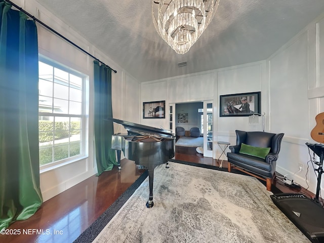 living area with a chandelier, a textured ceiling, wood finished floors, and a decorative wall