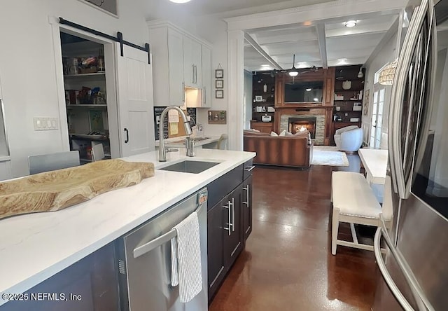 kitchen with finished concrete flooring, a barn door, appliances with stainless steel finishes, a sink, and a lit fireplace