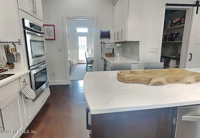 kitchen with double oven, light stone counters, baseboards, white cabinets, and tasteful backsplash