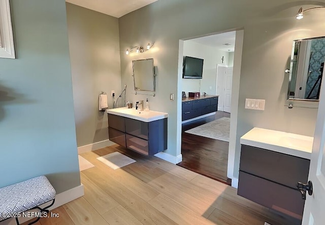 full bath with a sink, baseboards, two vanities, and wood finished floors