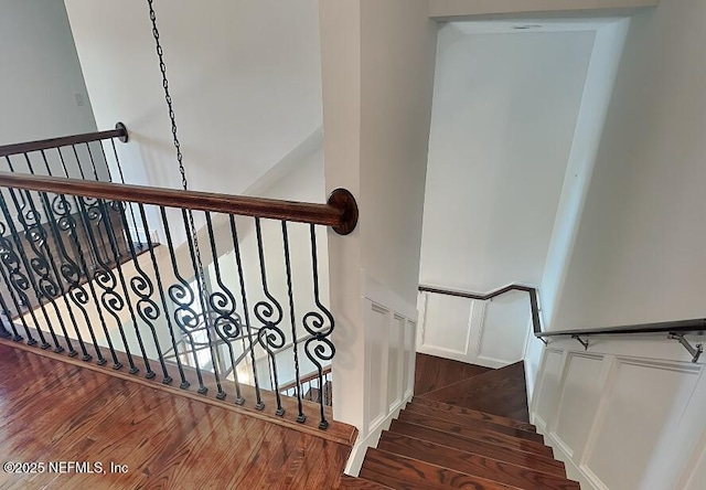 staircase with a wainscoted wall, wood finished floors, and a decorative wall