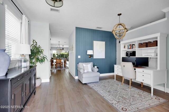 office area with light wood-type flooring, visible vents, baseboards, and a chandelier