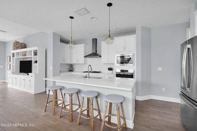 kitchen featuring wood finish floors, stainless steel appliances, visible vents, and wall chimney range hood