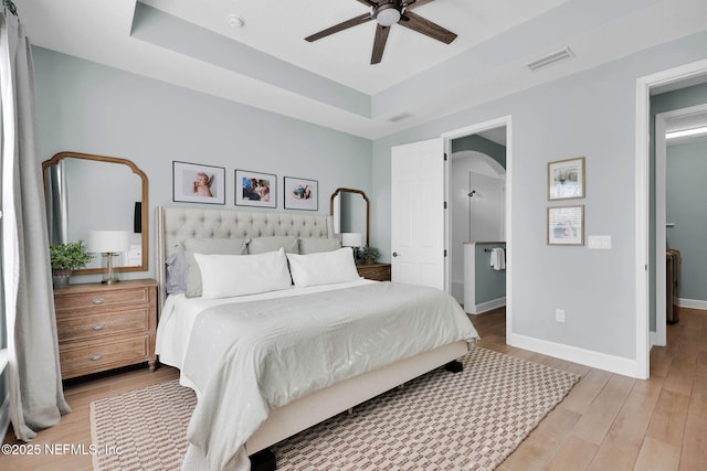 bedroom with a raised ceiling, light wood-style floors, visible vents, and baseboards