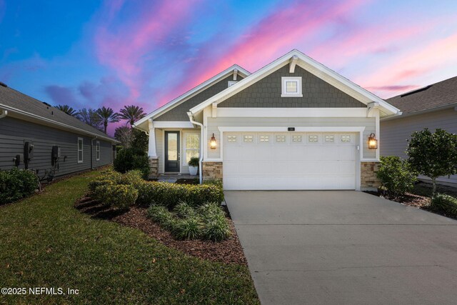 craftsman-style house with a yard, stone siding, concrete driveway, and an attached garage