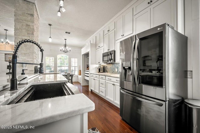 kitchen with a notable chandelier, backsplash, appliances with stainless steel finishes, dark wood-type flooring, and a sink