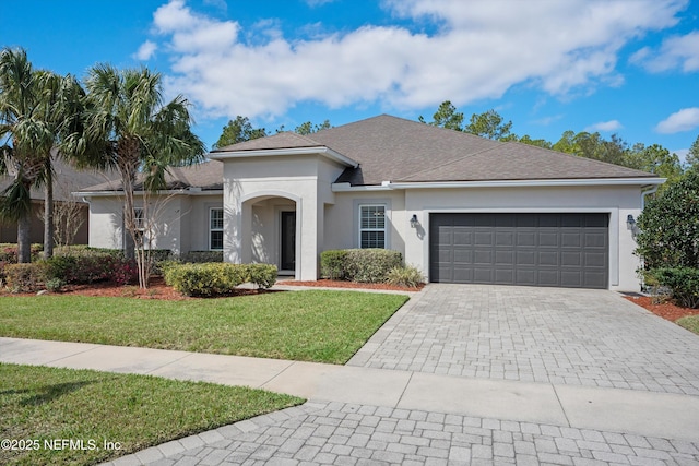 single story home featuring a garage, a shingled roof, decorative driveway, a front lawn, and stucco siding