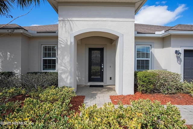 doorway to property with an attached garage, roof with shingles, and stucco siding