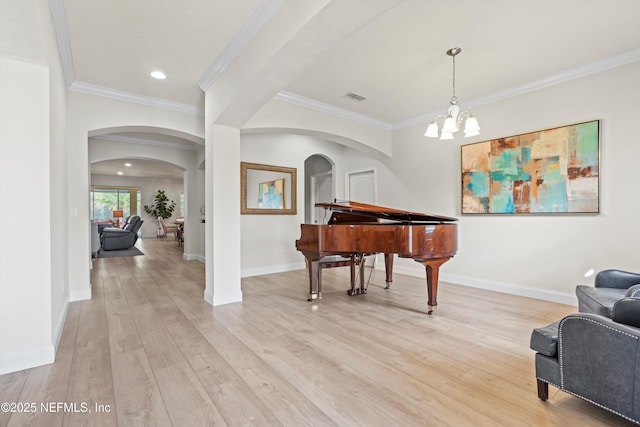 living area featuring light wood-type flooring, crown molding, arched walkways, and baseboards