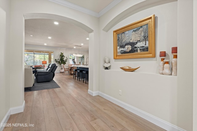 corridor with arched walkways, recessed lighting, light wood-style floors, ornamental molding, and baseboards