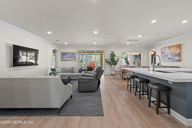 living area featuring arched walkways, crown molding, light wood-style floors, a textured ceiling, and baseboards