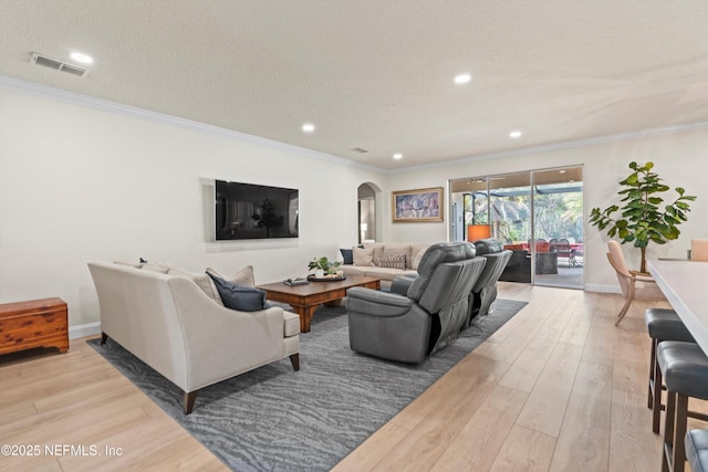 living room featuring arched walkways, visible vents, ornamental molding, a textured ceiling, and wood finished floors