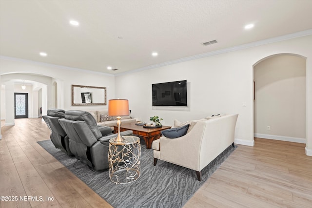 living room with arched walkways, crown molding, visible vents, light wood-style floors, and baseboards