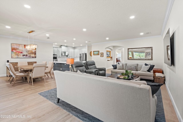 living room featuring arched walkways, crown molding, light wood finished floors, visible vents, and a textured ceiling