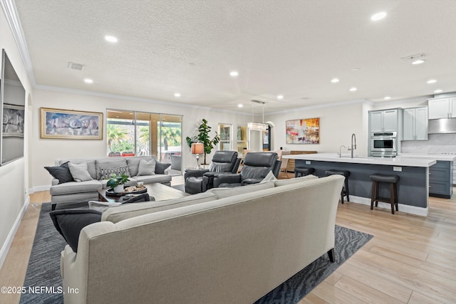 living room with visible vents, ornamental molding, a textured ceiling, light wood-style floors, and recessed lighting