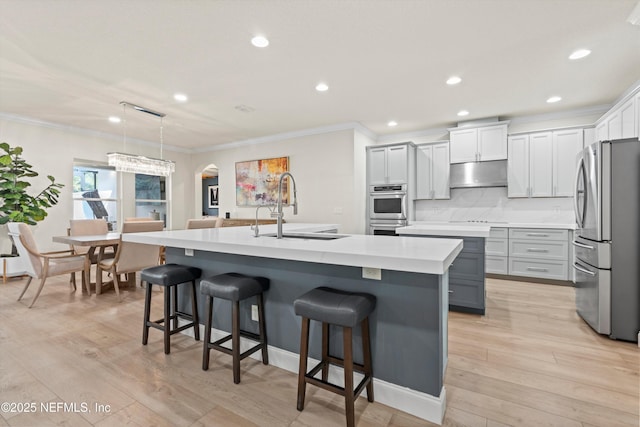 kitchen featuring under cabinet range hood, stainless steel appliances, a sink, hanging light fixtures, and an island with sink