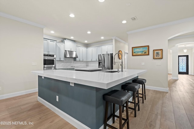 kitchen featuring arched walkways, visible vents, appliances with stainless steel finishes, a kitchen bar, and a large island with sink