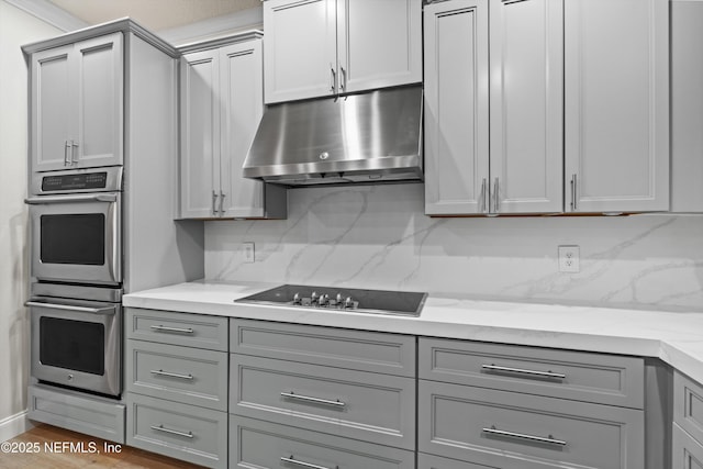 kitchen featuring stainless steel double oven, black electric stovetop, under cabinet range hood, and gray cabinetry