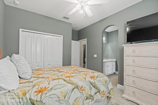 bedroom with arched walkways, ensuite bathroom, light colored carpet, visible vents, and a closet